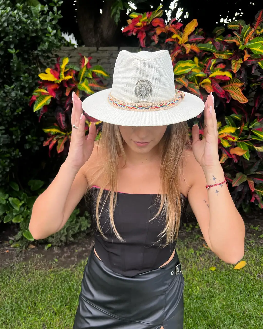 Modelo con sombrero blanco de banda trenzada multicolor entre plantas