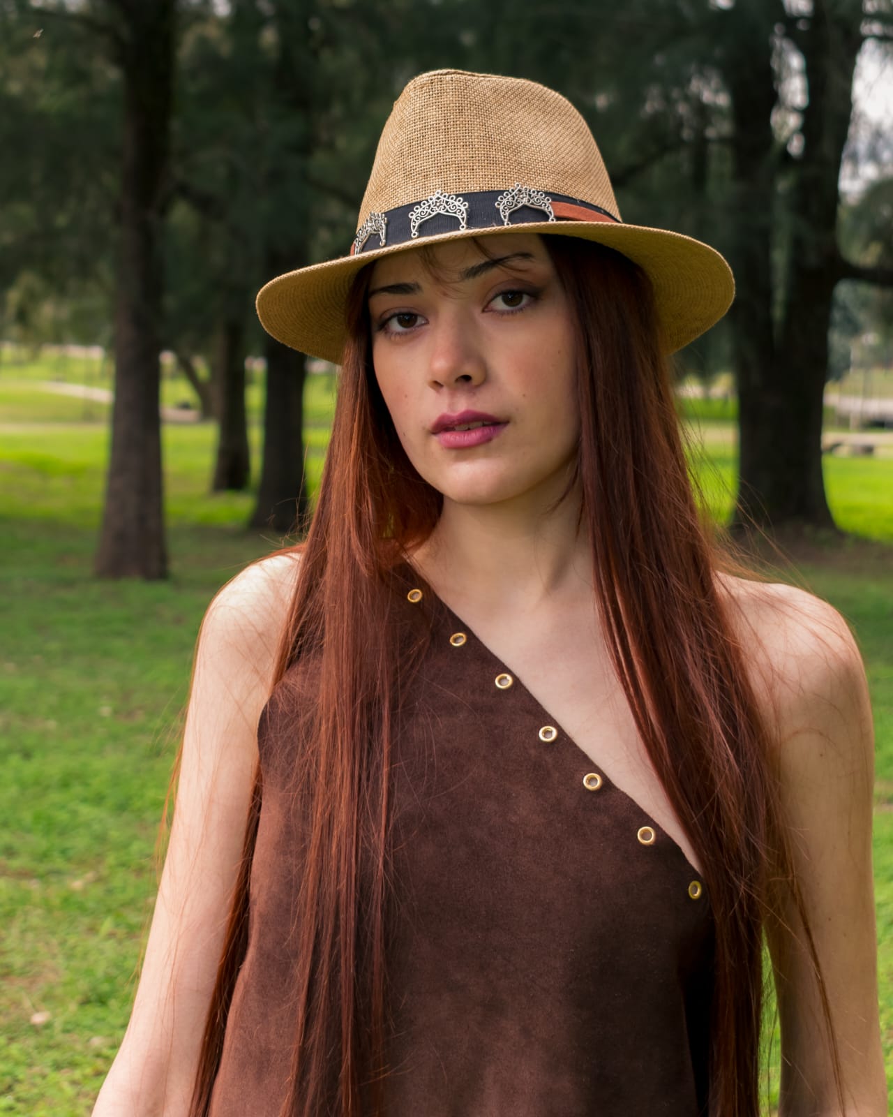 Sombrero de fibra natural con banda de dijes metálicos, sobre una modelo