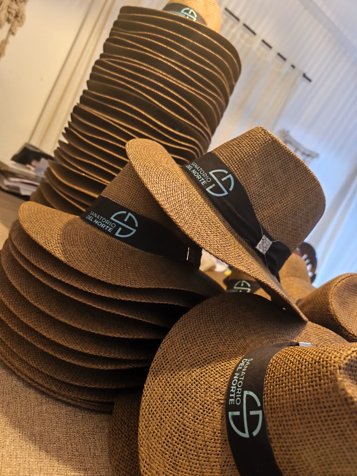 Pila de sombreros de fibra con banda negra y logo de empresa estampado, listos para un evento corporativo